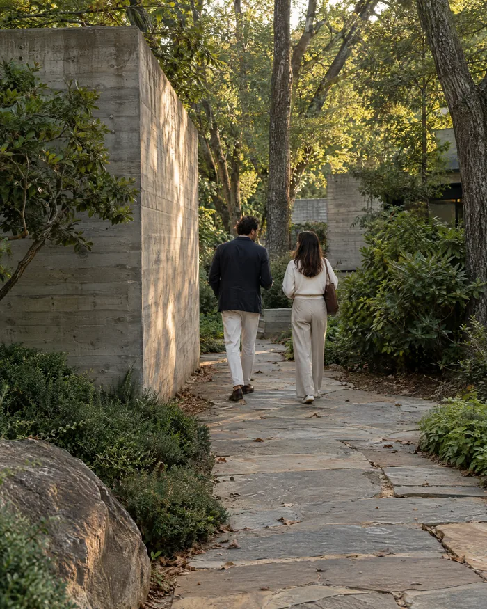 Two people walking and talking along a stone path through a green garden.