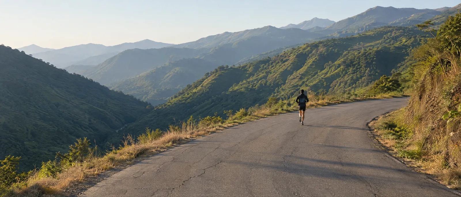 A runner on a quiet mountain road through green hills in morning light.